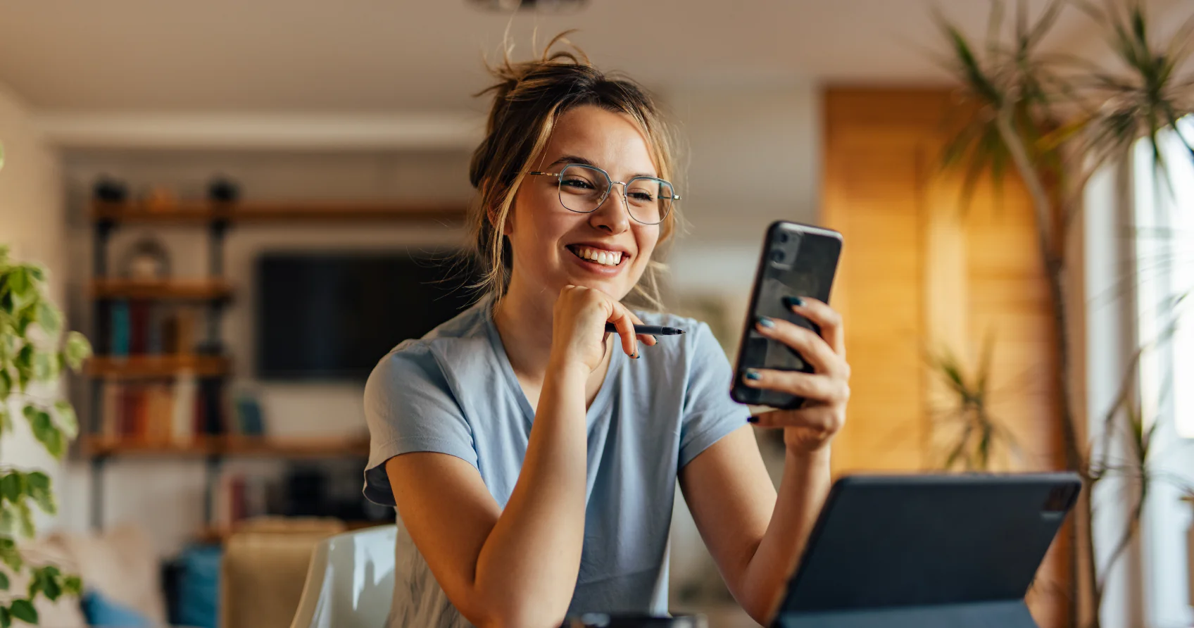 A woman is sitting at her desk looking at her phone smiling.